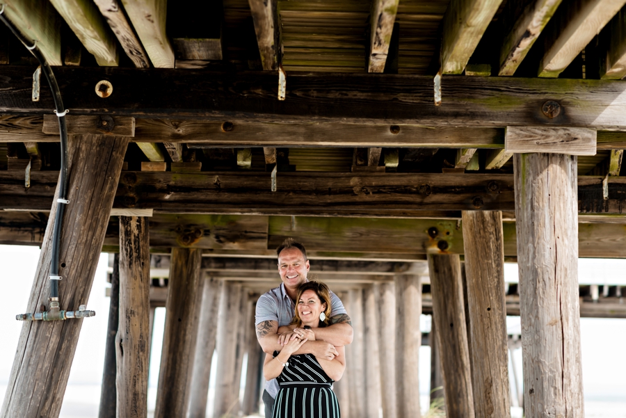 An engaged couple embrace under the pier in cape may.